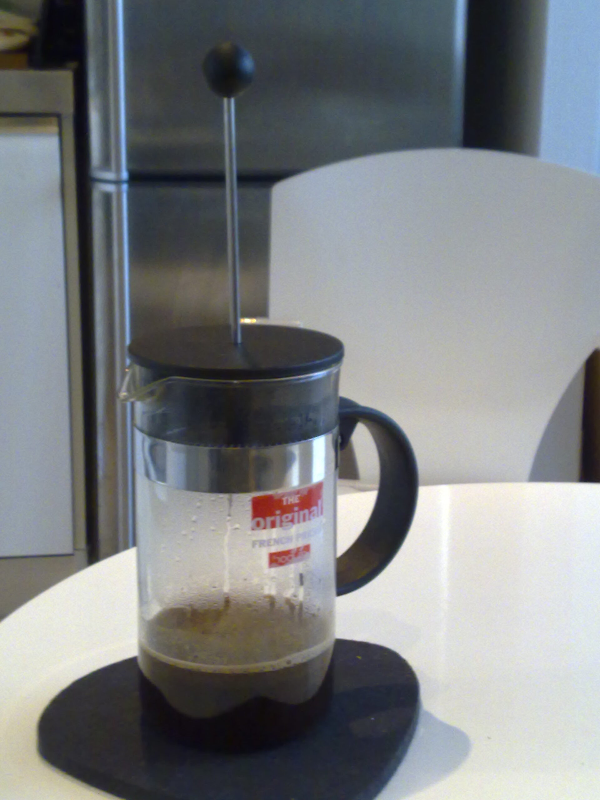 Coffee steeping inside a glass Bodum French press with its plunger raised.