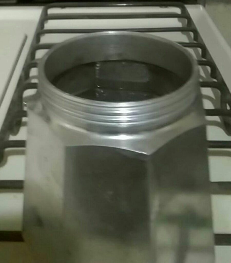 Water being poured into the lower chamber of a disassembled moka pot.