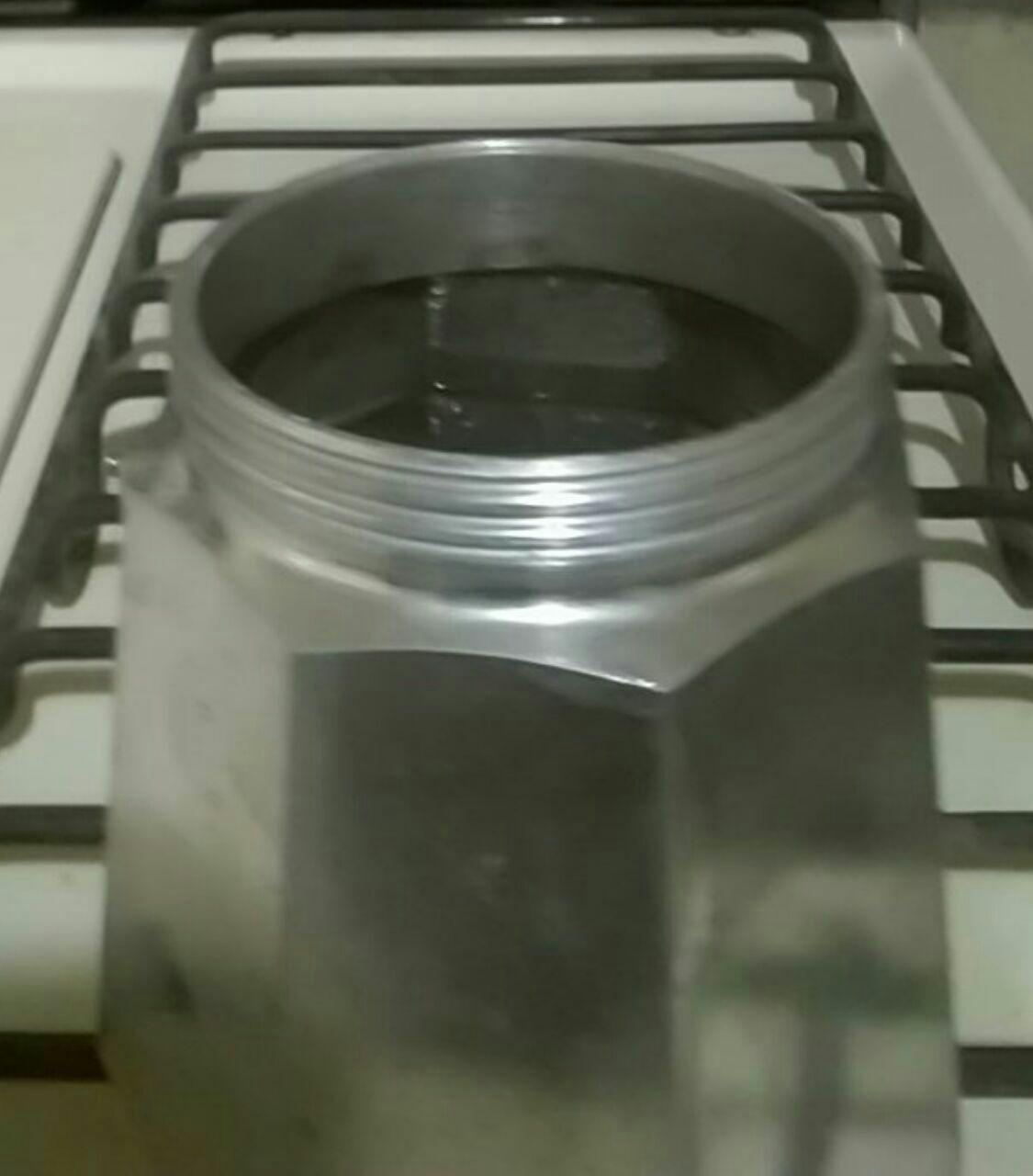 Water being poured into the lower chamber of a disassembled moka pot.